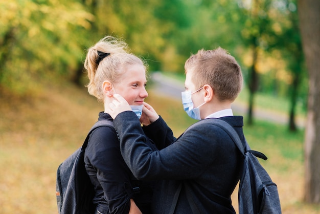 Schoolchildren, a boy and girl in medical masks walk in the city park.