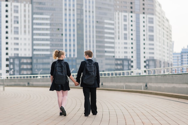 医療用マスクを身に着けた男の子と女の子の学童が街を歩きます。