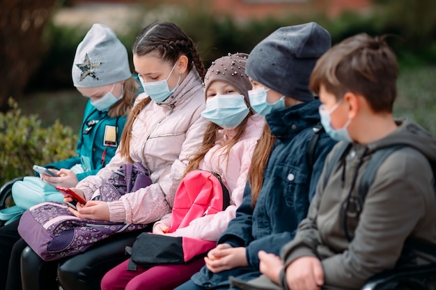 Schoolgaande kinderen in medische maskers zitten op een bankje.