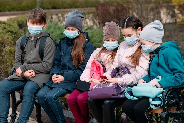 Schoolgaande kinderen in medische maskers zitten op een bankje.