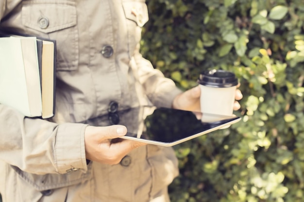 Schoolgirl carrying tablet cup of coffee and books
