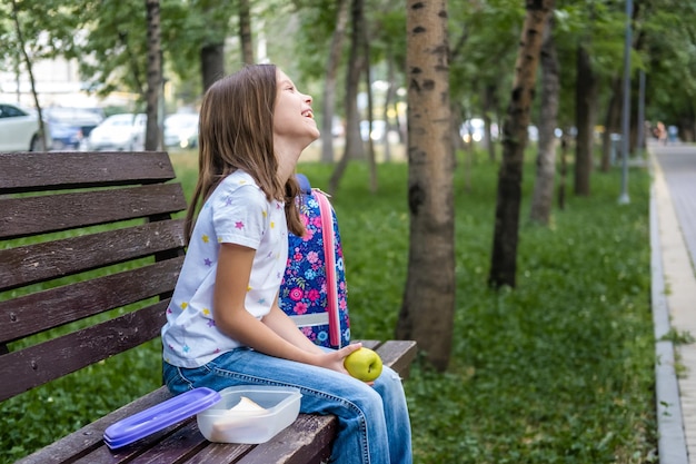 Schoolgirl child eating lunch sandwich and apple in park