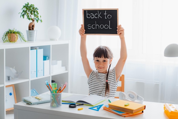 Schoolgirl girl doing homework happily raises a blackboard with the inscription back to school