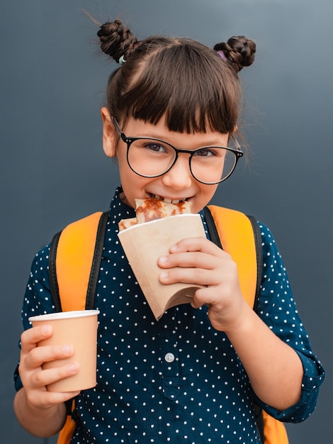 Foto ragazza studentessa con gli occhiali in pausa pranzo su sfondo grigio pasti scolastici fast food sano per i bambini