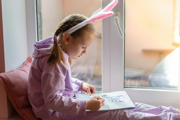 a schoolgirl girl with rabbit ears sits on the window and draws a rabbit in her album