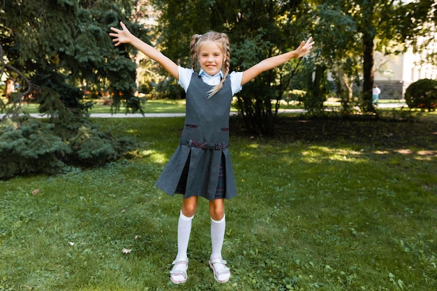 A schoolgirl goes to school with raised hands on the background of the park. girl in school uniform in the park.