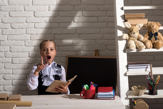 Schoolgirl has idea holding open book near blackboard