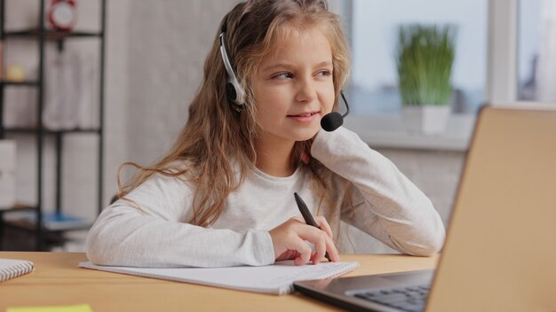 Schoolgirl in headset has online lesson, video call with teacher, answering questions,check of knowledge.