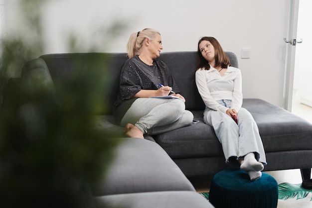 A schoolgirl and her mother are sitting on the couch doing their homework and laughing happily
