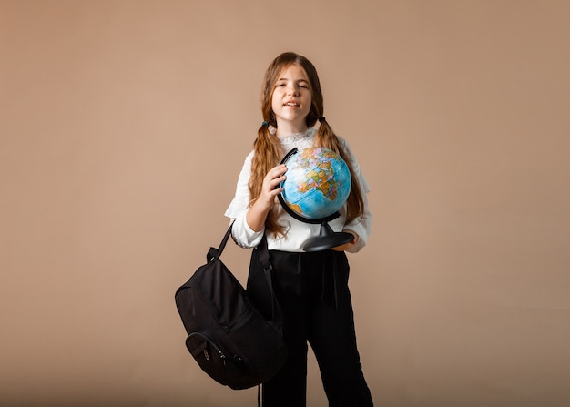 Schoolgirl holding globe, showing with finger blank space, isolated on studio background