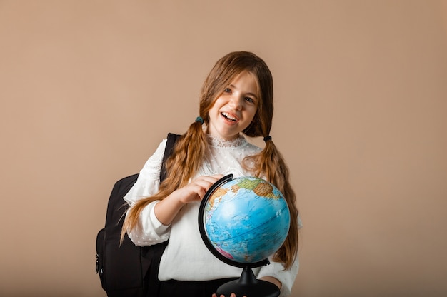 Schoolgirl holding globe, showing with finger blank space, isolated on studio background