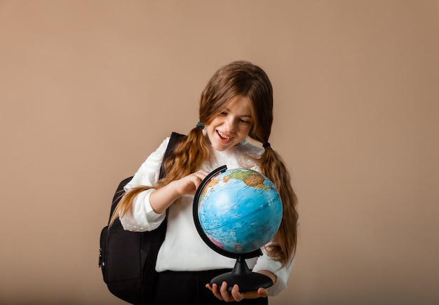 Schoolgirl holding globe, showing with finger blank space, isolated on studio background