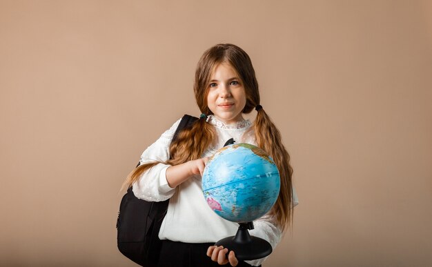 Schoolgirl holding globe, showing with finger blank space, isolated on studio background