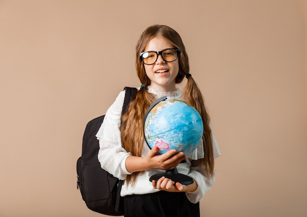 Schoolgirl holding globe, showing with finger blank space, isolated on studio background