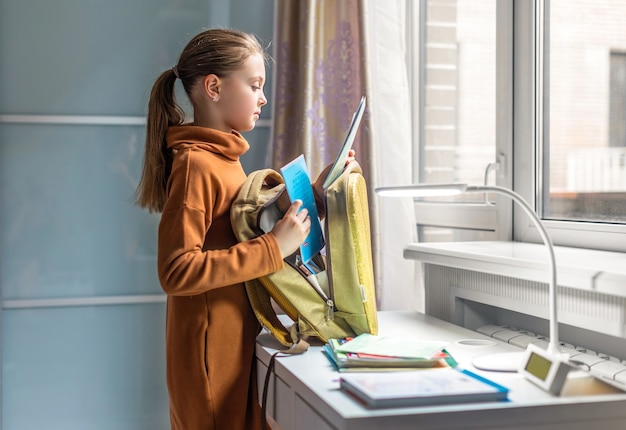 Foto la scolaretta a casa sta andando a scuola. il bambino raccoglie uno zaino. di nuovo a scuola. preparazione per la scuola.