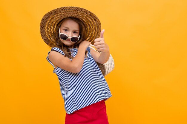 Schoolgirl is going on a trip, photo of a girl in a beach hat on a yellow background