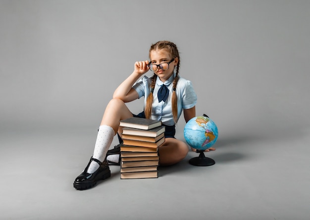 Schoolgirl isolated on yellow background with globe. little girl in school uniform sitting on a yellow background, reading a book. blonde girl in school uniform on a yellow background