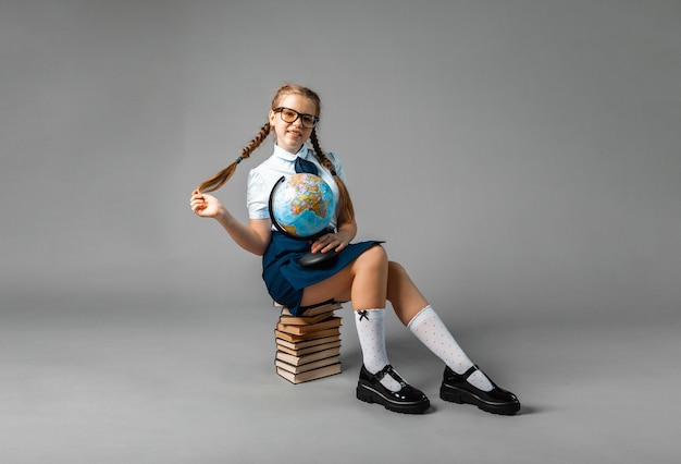 Foto studentessa isolata su sfondo giallo con globo. bambina in uniforme scolastica seduta su uno sfondo giallo, leggendo un libro. ragazza bionda in uniforme scolastica su sfondo giallo