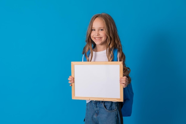 schoolgirl in jeans and a white T-shirt with a backpack holds a white writing board in her hands