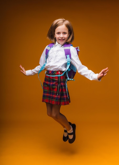 Schoolgirl jumping high rejoicing at the return school clothes casual plaid skirtisolated yellow background