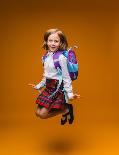 Schoolgirl jumping high rejoicing at the return school clothes casual plaid skirtisolated yellow background