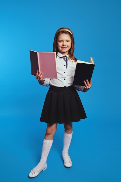 Schoolgirl learns information from textbook poses over blue background