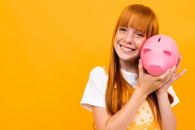 Schoolgirl on an orange hugs a piggy bank in the form of a pink pig