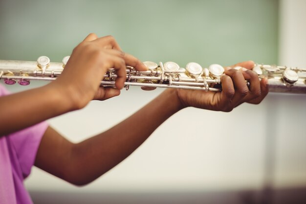 Schoolgirl playing flute in classroom