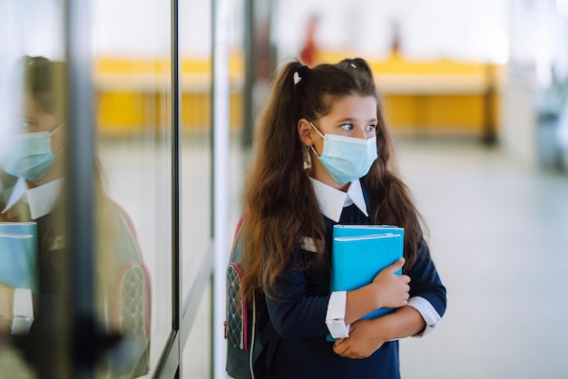 Scolara in una maschera protettiva con uno zaino e un libro di testo