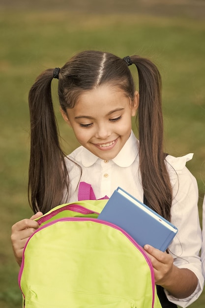 Schoolgirl putting book inside backpack ready for lessons concept