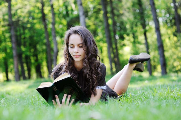 Schoolgirl reading a book sitting on the grass. Beautiful girl reading a book