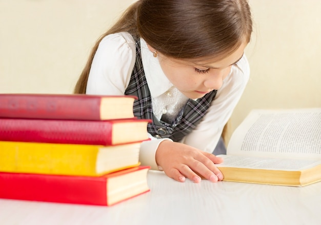 Schoolgirl reading a book at a table with a stack of books