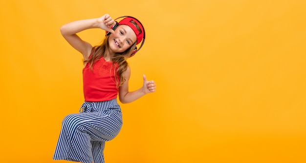 Schoolgirl in a red T-shirt and jeans dancing energetically on a yellow background, emotional portrait