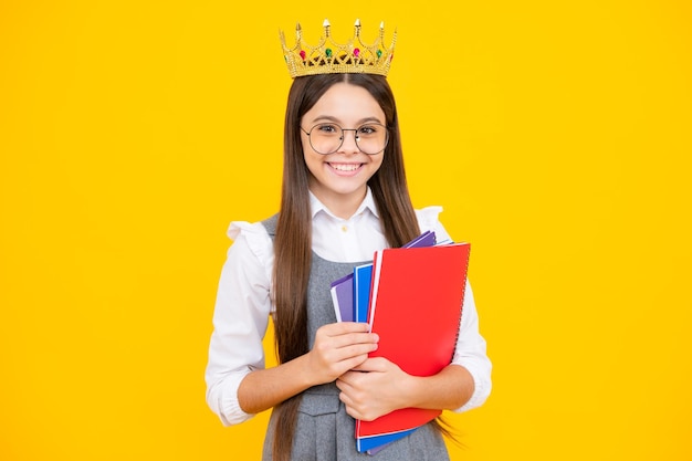 Schoolgirl in school uniform and crown celebrating victory on yellow background school child hold books education graduation victory and success