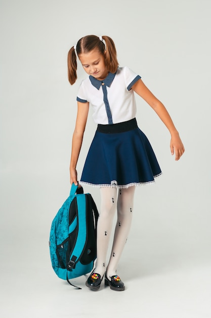 Schoolgirl in school uniform holding a heavy backpack. The problem of weighting student accessories