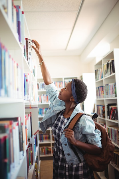 Schoolgirl selecting book from book shelf in library