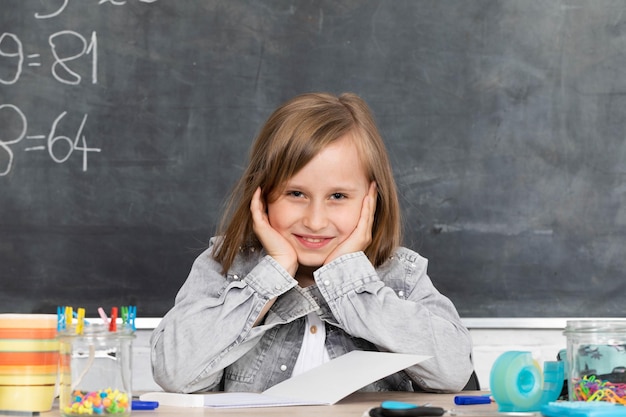 The schoolgirl sits at a school bench and supports her head with her hands in anticipation of a teacher