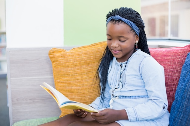 Schoolgirl sitting on sofa and reading book