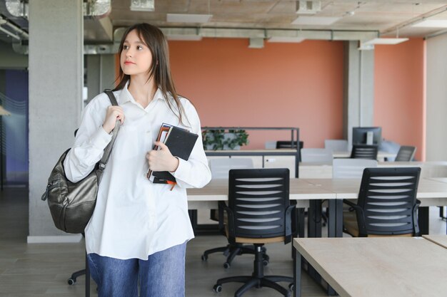 写真 学校で本とバックパックを持って立っている女子高生