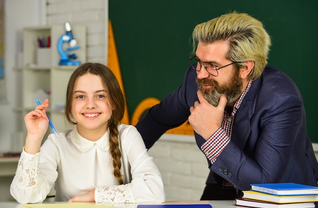 Studentessa che studia. di nuovo a scuola. bambina e uomo contro la lavagna. concetto di giorno della conoscenza. bambino con insegnante in classe a scuola. buona giornata degli insegnanti. insegnante e studentessa a lezione.