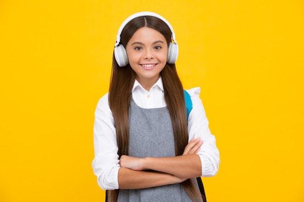 Schoolgirl teenage student girl in headphones on yellow isolated studio background School and music education concept Back to school Happy girl face positive and smiling emotions