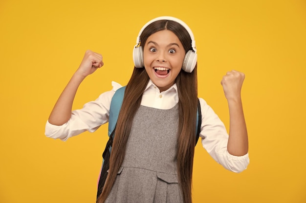 Schoolgirl teenage student girl in headphones on yellow isolated studio background School and music
