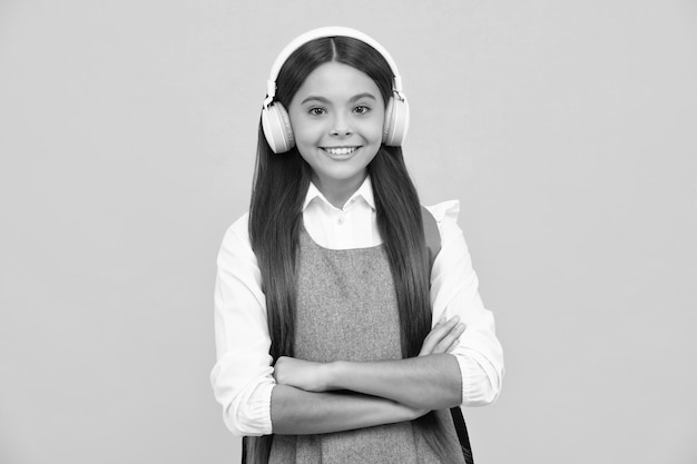 Schoolgirl teenage student girl in headphones on yellow isolated studio background school and music