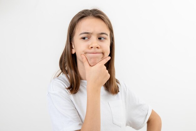 A schoolgirl thoughtfully holds her hand near her face on a white background