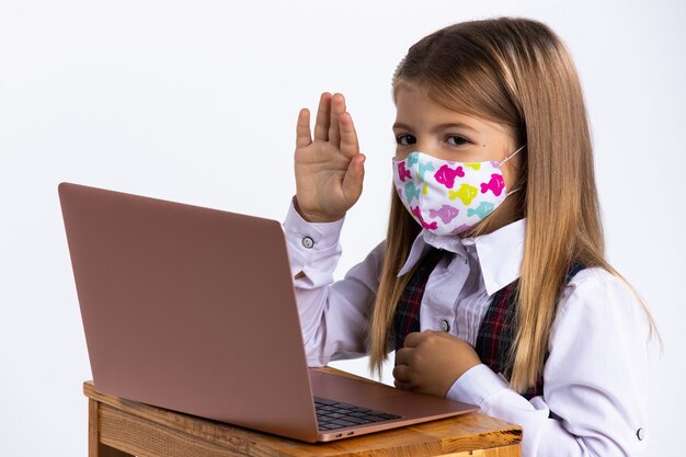 Schoolgirl wearing face protective mask with hand up sits in her desk at school after covid-19. Isolation- school social distance. Quarantine and lockdown.. 