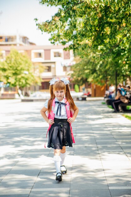 A schoolgirl in a white blouse and a black skirt with a\
briefcase is walking down an alley or down the street.the girl goes\
to school or home after school.