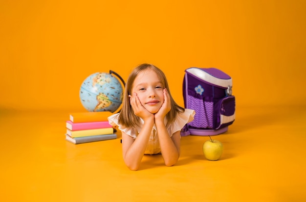 Schoolgirl in a white blouse lies with school supplies and a globe on a yellow background with a copy of the space