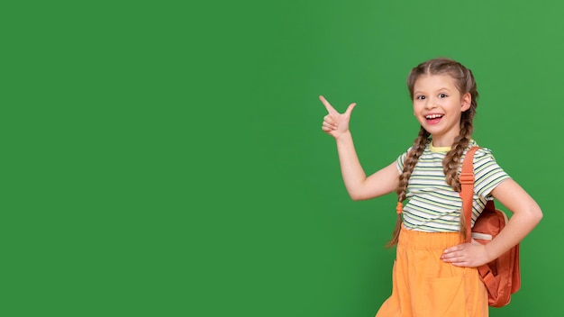 A schoolgirl with a briefcase points her finger up at the advertisement. green isolated background. copy space. secondary school education.