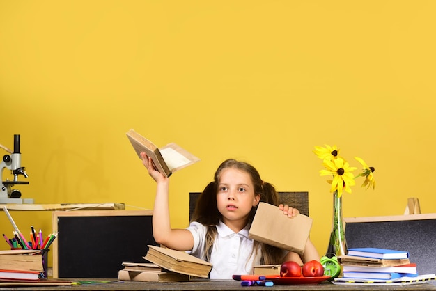 Schoolgirl with face draws in art book Kid and school supplies on yellow wall background