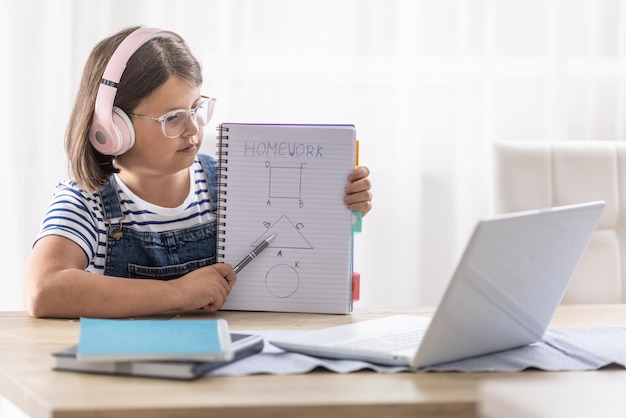 La studentessa con le cuffie mostra i suoi compiti all'insegnante durante una lezione online tramite computer